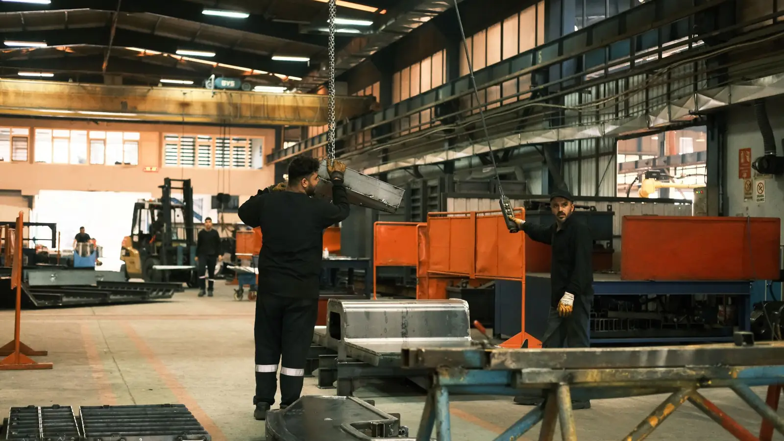 Workers moving steel through a fabrication plant under overhead cranes