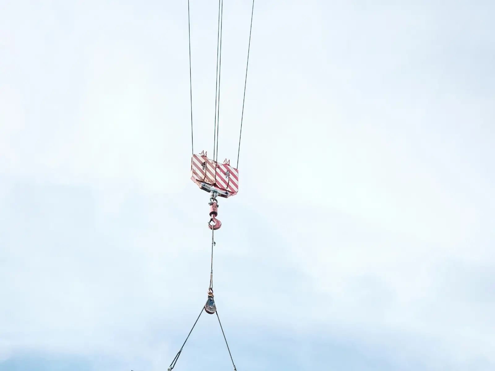 A precast wall panel hanging from a crane hook in a pale sky
