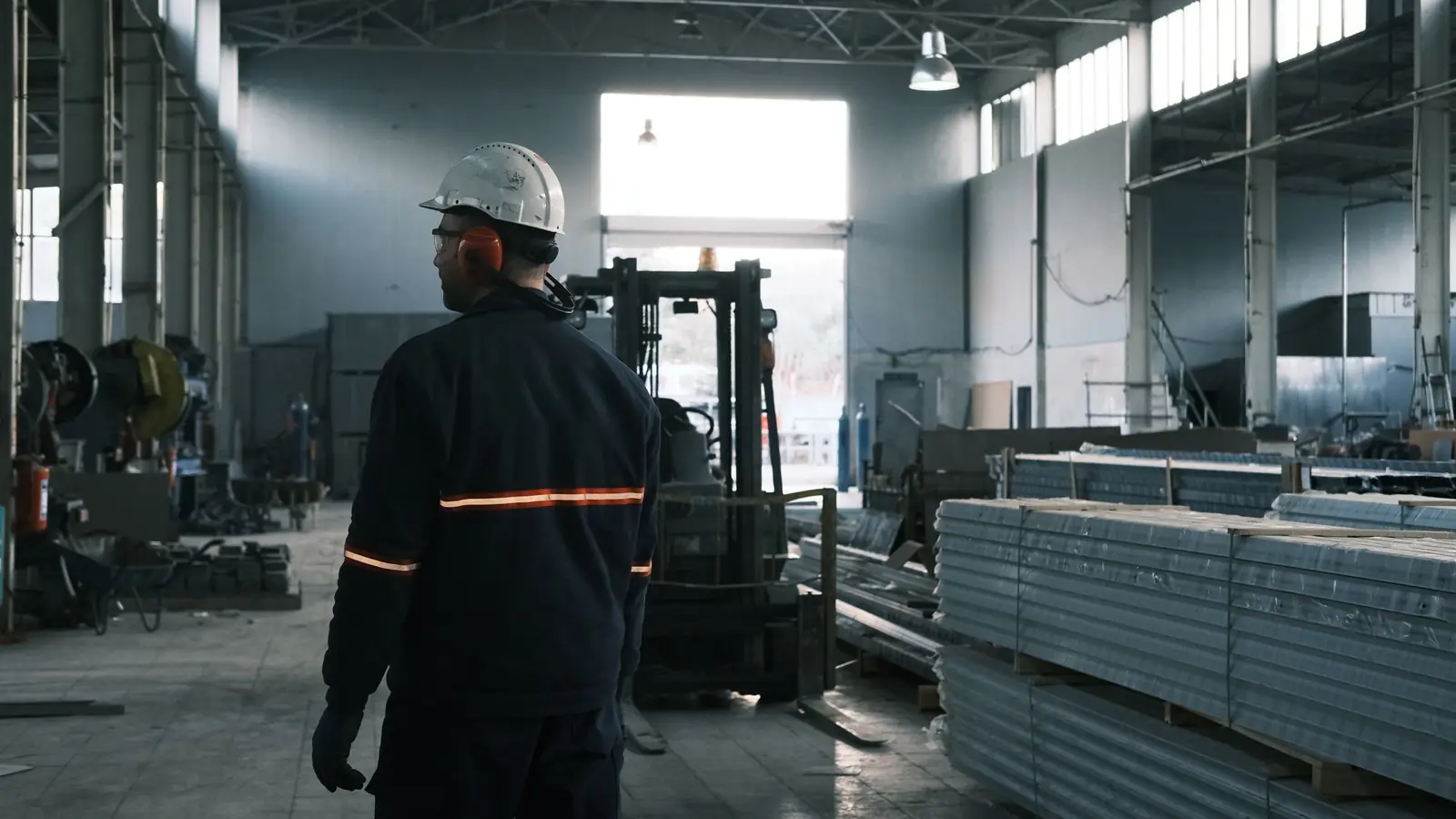 A worker in a hard hat walking the floor of a metal fabrication plant