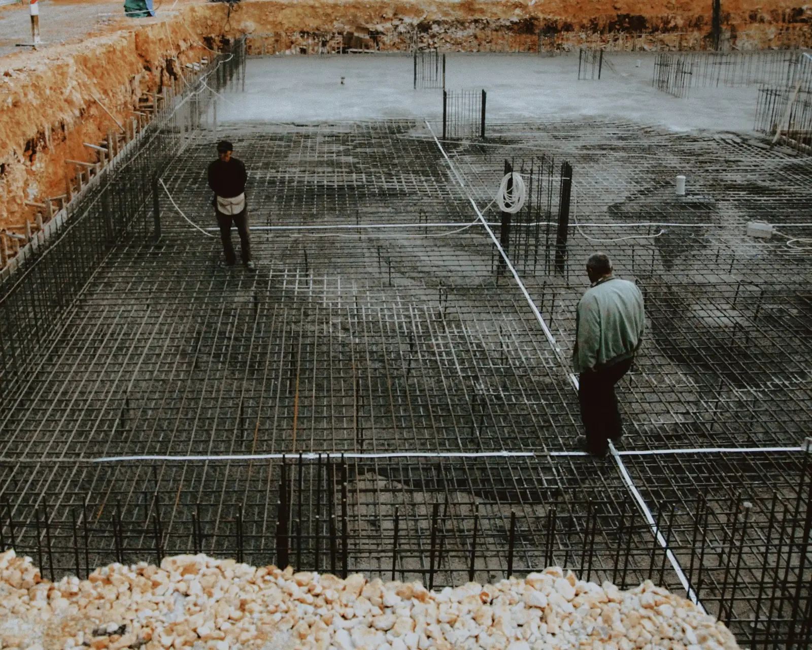 Two workers checking a rebar grid before a foundation pour