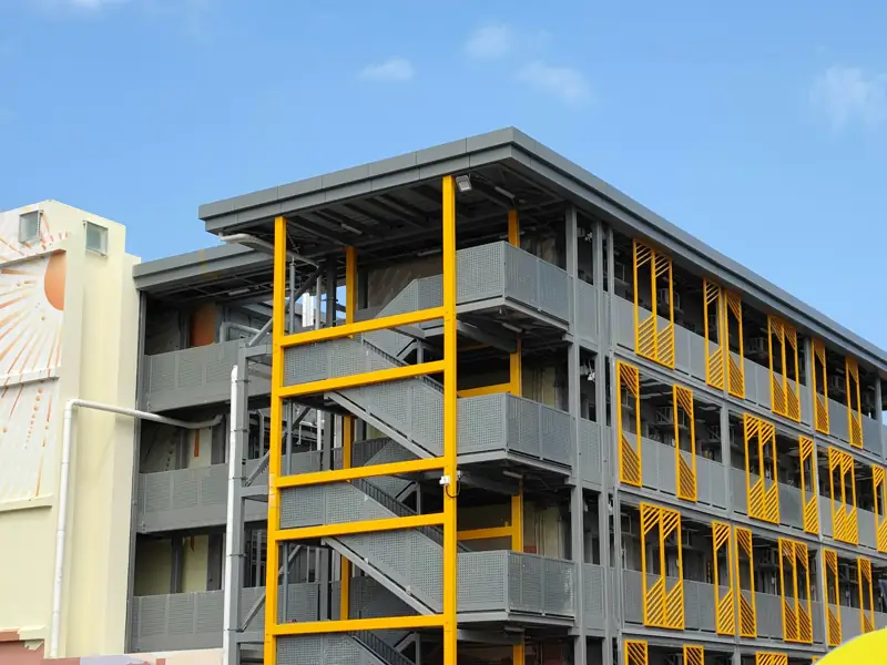 Crews in hard hats at the base of a new four-storey steel-framed building with yellow stair towers