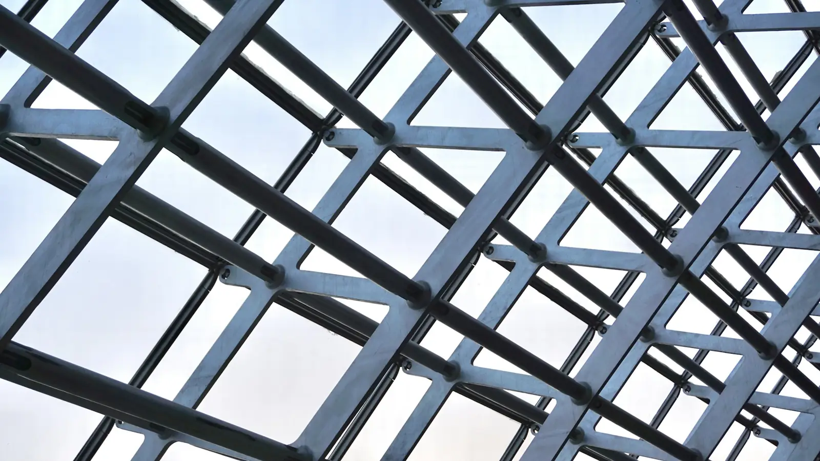 Looking up through a grid of steel framing members against the sky