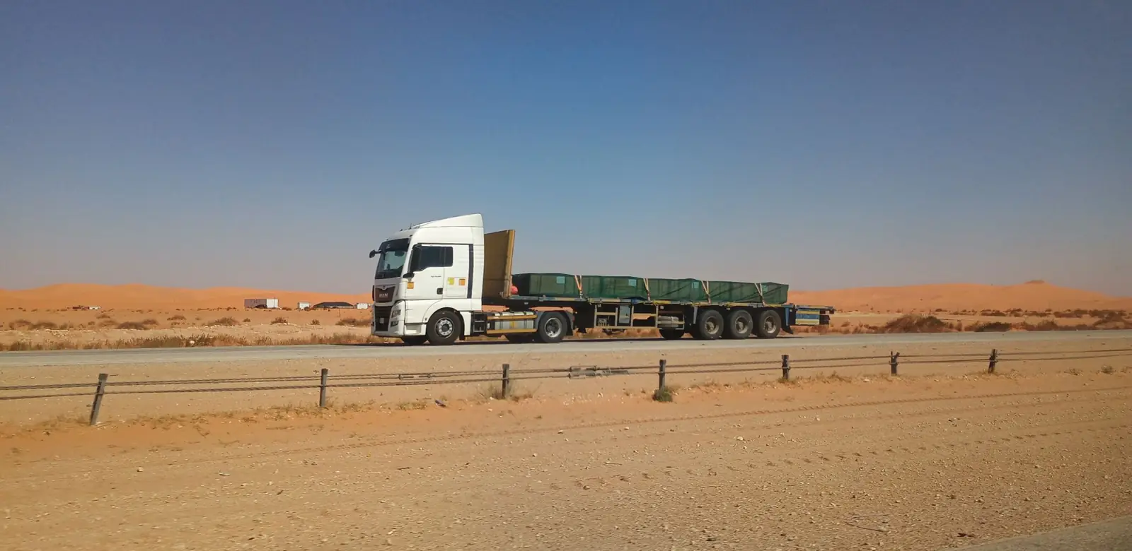 A flatbed truck hauling a long load across open desert